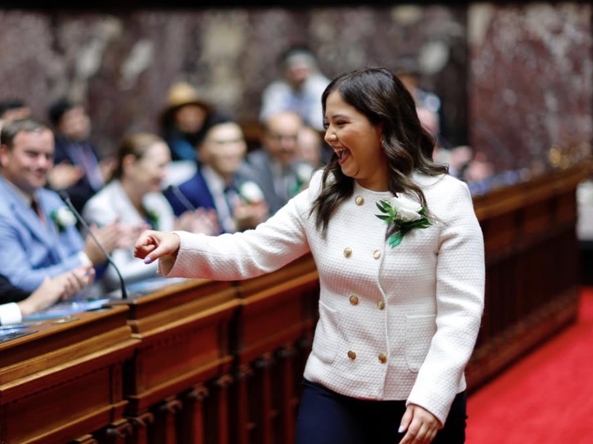 Amna Shah, wearing a white jacket, greets someone on the floor of the B.C. Legislature chamber.